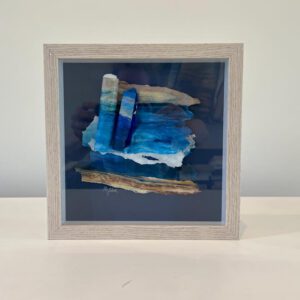 Available, July 2025. A framed piece of sea glass in a white frame.