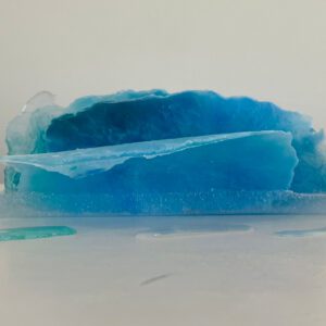 Available, July, 2025. A translucent blue resin sculpture resembling an ice formation, displayed on a white surface with droplets around it.